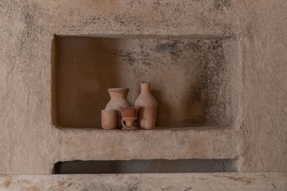 Interior of a Tlaxco pulquería: wooden tables and clay vessels, curados in glass jars, a woman serving behind the counter