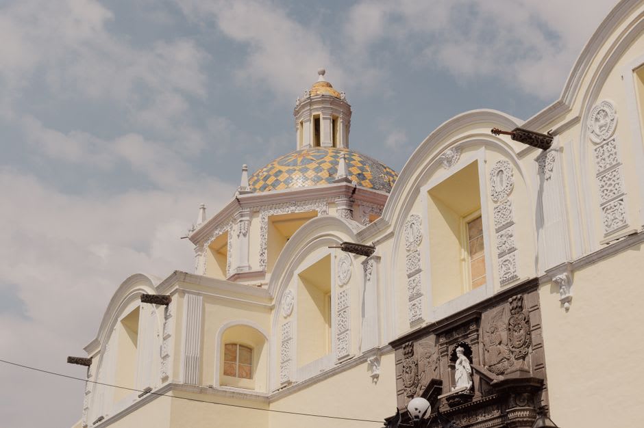 The exterior facade of Santa María Tonantzintla with its cream-colored baroque towers and dome under a blue Puebla sky
