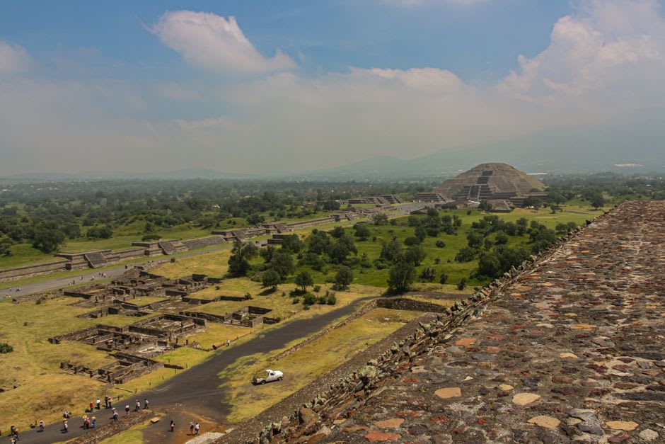 View from the upper platforms of Toniná looking down the terraced complex toward the green Valle de Ocosingo, cloud shadows crossing the valley floor