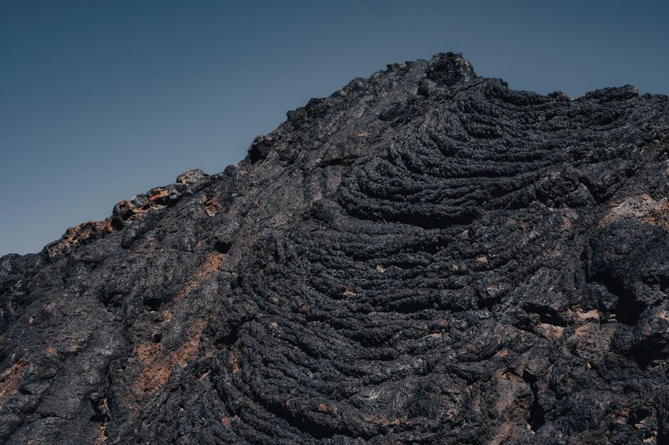 The ruined facade and bell tower of the San Juan Parangaricutiro church emerging from the hardened lava field of Paricutín volcano, the black basalt surrounding the 16th-century stone structure, the volcanic cone visible behind
