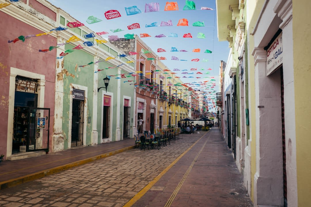 Colorful colonial buildings lining a quiet street in Valladolid, their painted facades in ochre, blue, and terracotta typical of the Yucatán peninsula