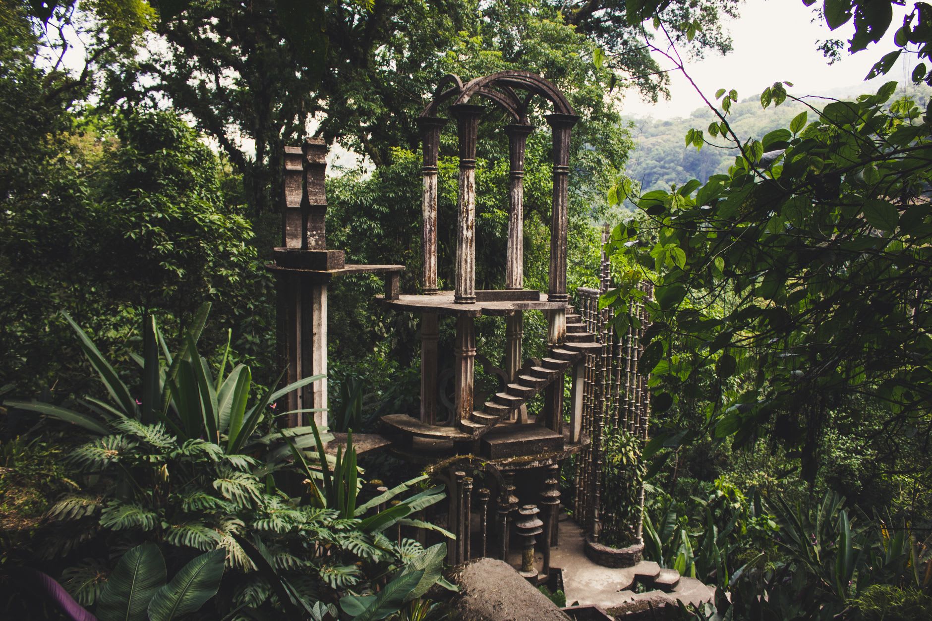 A spiral concrete staircase at Las Pozas rising through cloud forest, the steps ending in open air fifteen meters up, ferns and orchids growing from the cracks in the structure
