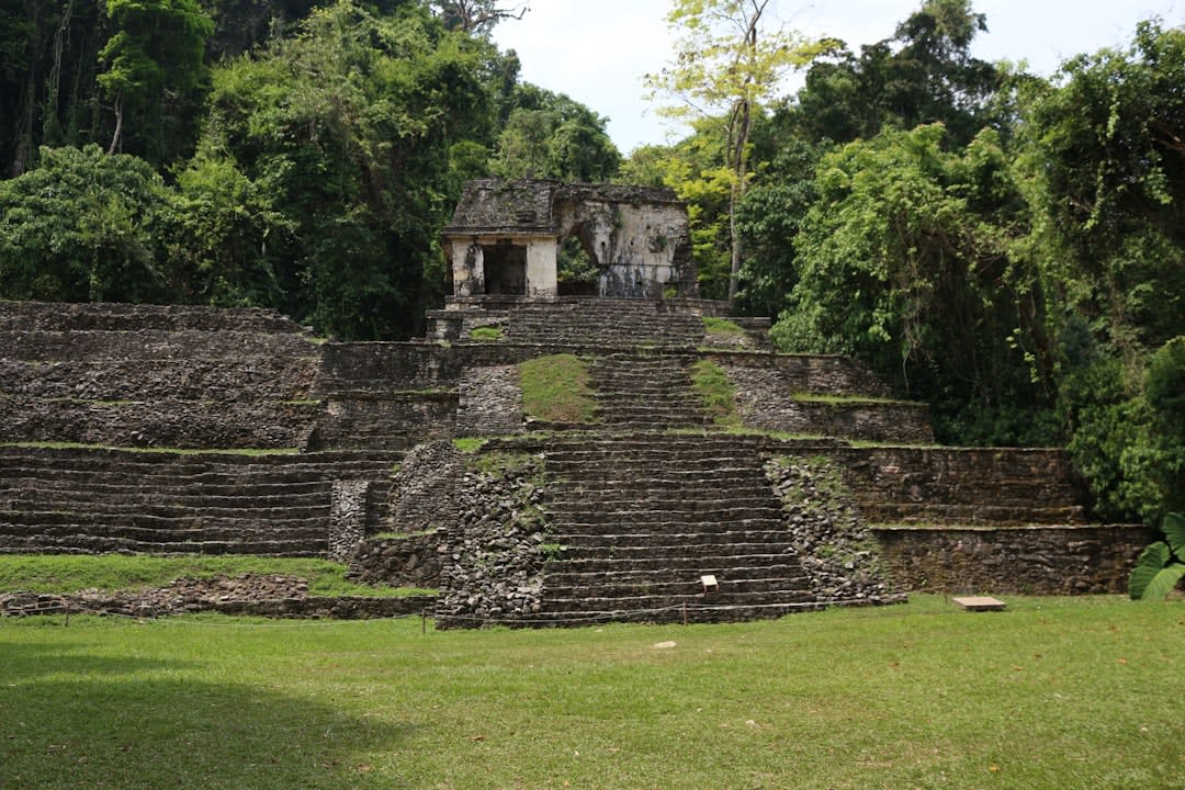 A carved stone lintel inside a Yaxchilán temple showing a Maya lord and lady in bloodletting ritual, the fine narrative relief sculpture visible in the temple doorway, the Lacandon jungle visible through the opening