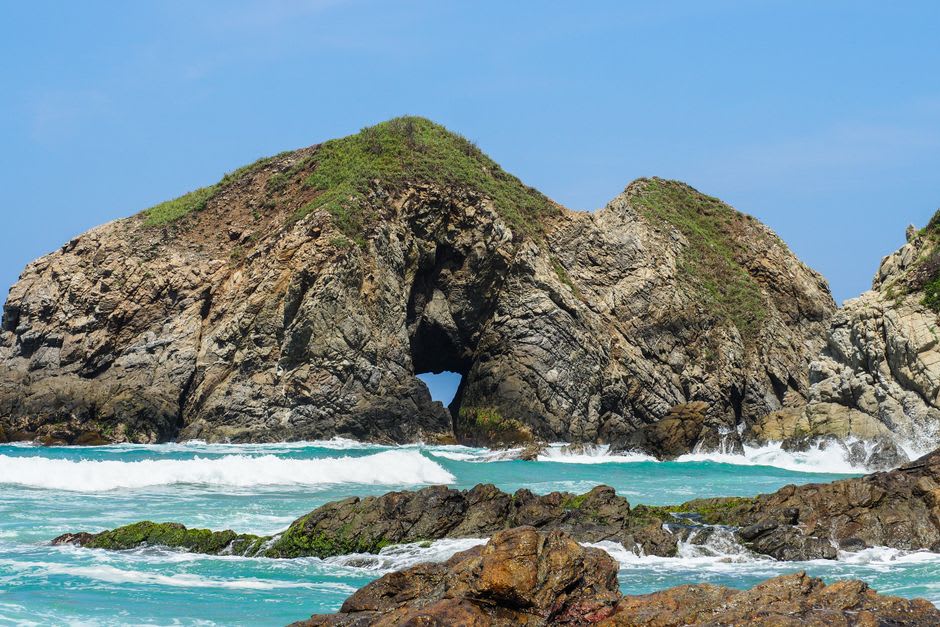 Skull and crossbones warning flag above Zipolite beach with the Pacific surf breaking behind it