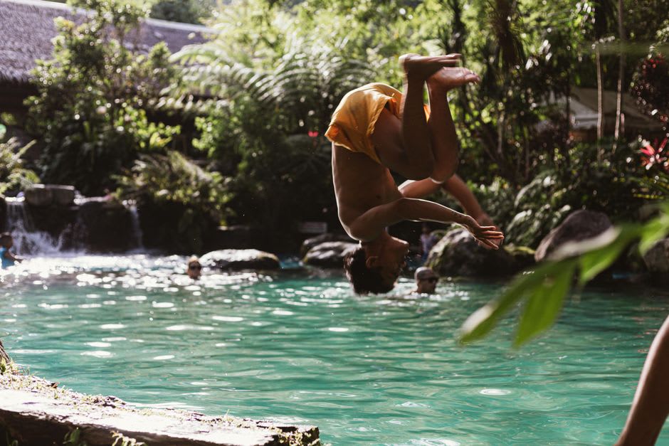 Local children swimming and diving into the dark pool at the base of Kepirohi Waterfall