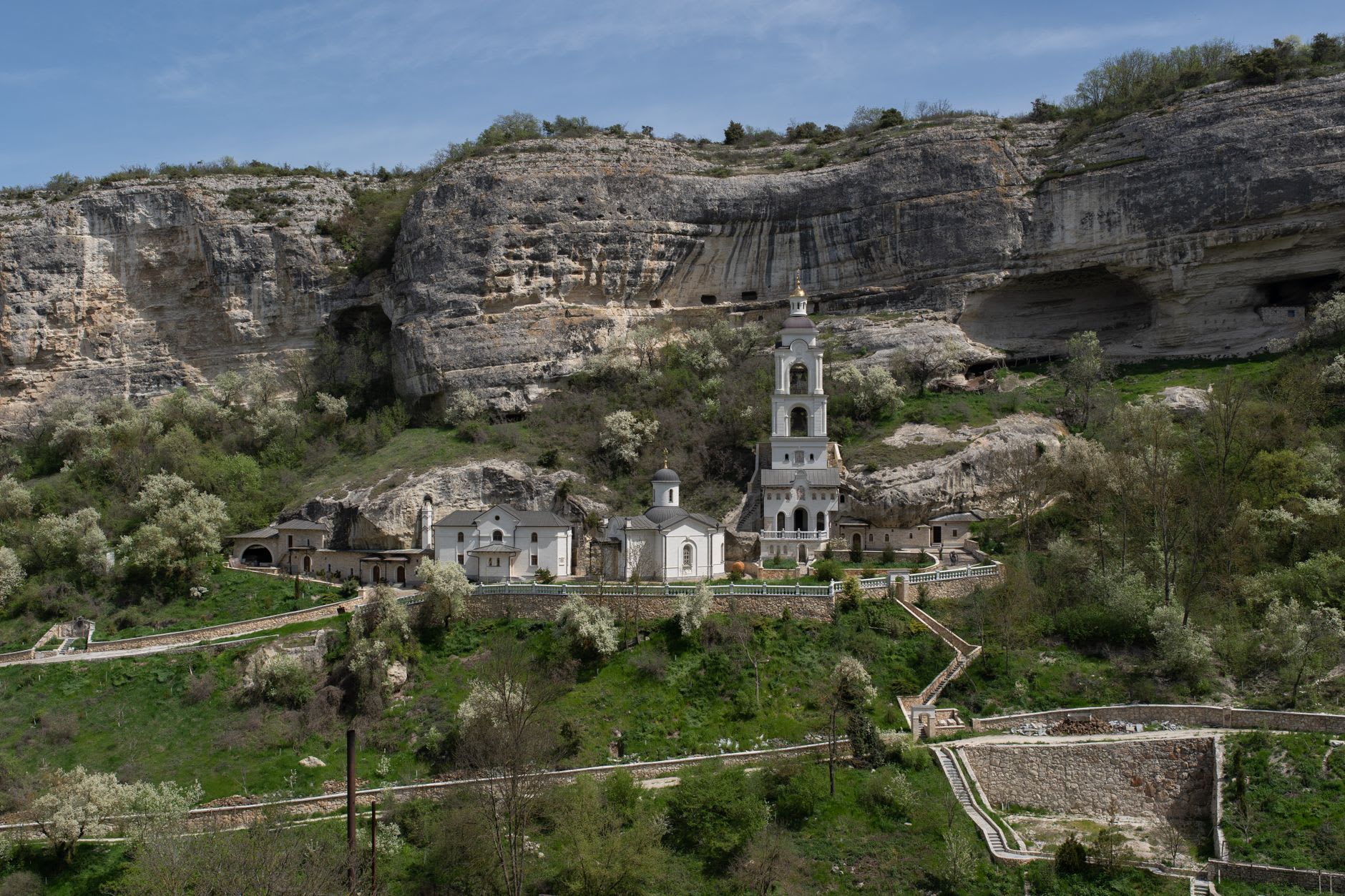 Ancho río Dniéster verde visto desde la orilla del agua bajo Rudi, acantilados de caliza y muros del monasterio elevándose a través del bosque de robles arriba, niebla matinal sobre el agua