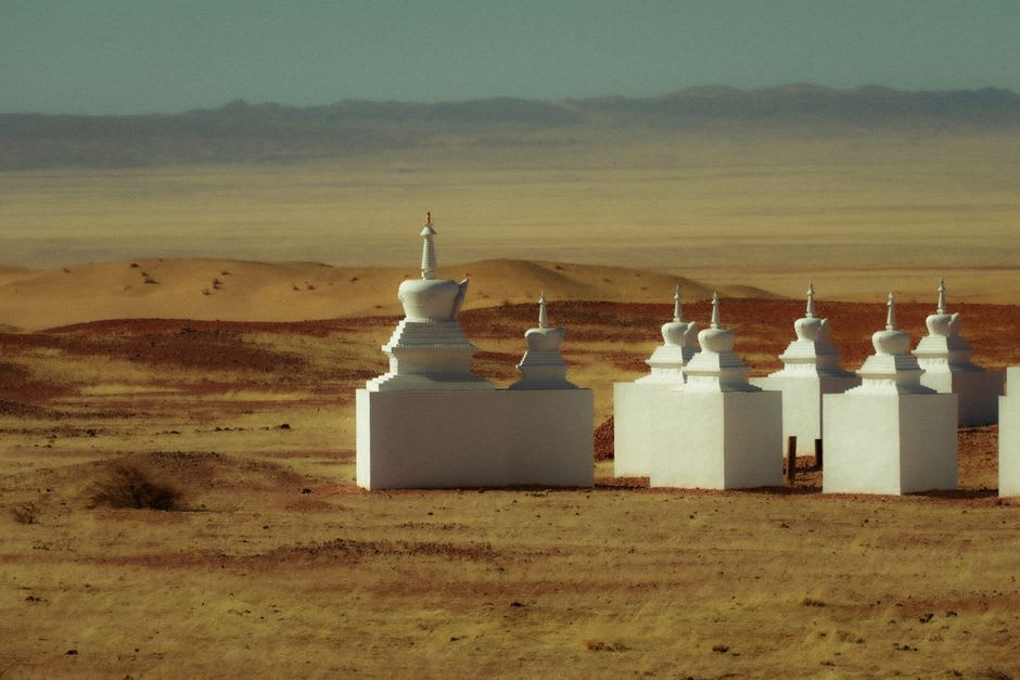 A small rebuilt temple with prayer flags standing among the wider field of monastery ruins
