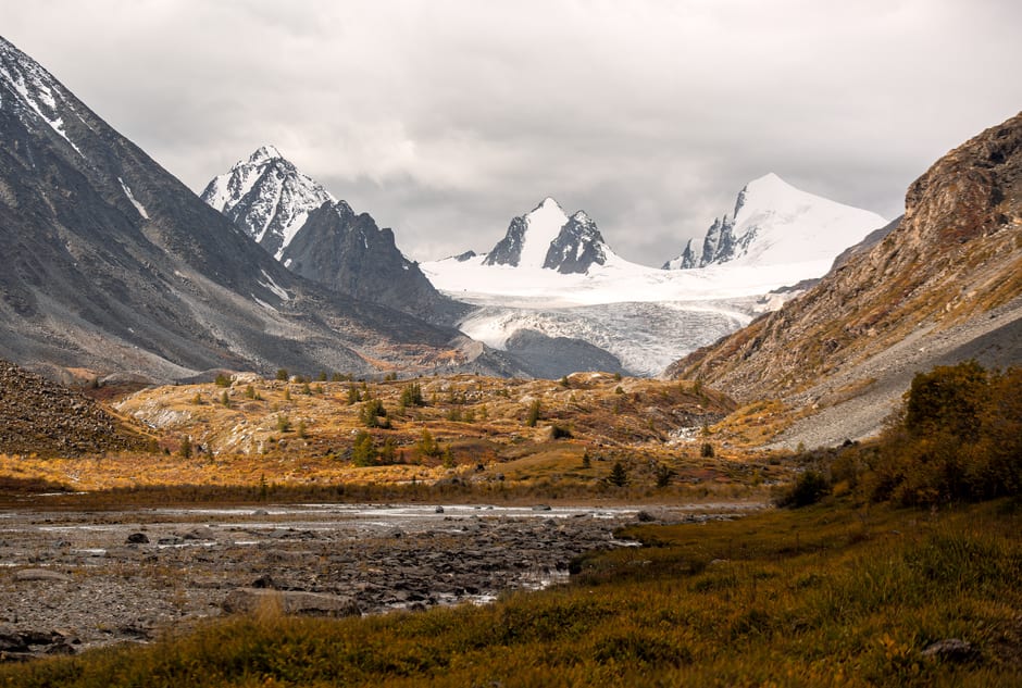 A high alpine valley in Altai Tavan Bogd National Park with a glacier-fed stream and distant snowy summits
