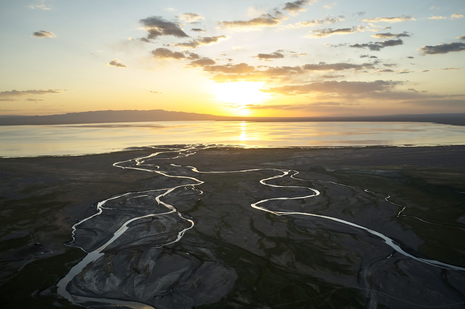 View across Terkhiin Tsagaan Lake at sunset, the water reflecting orange and gold, with a small fishing boat visible at the far shore