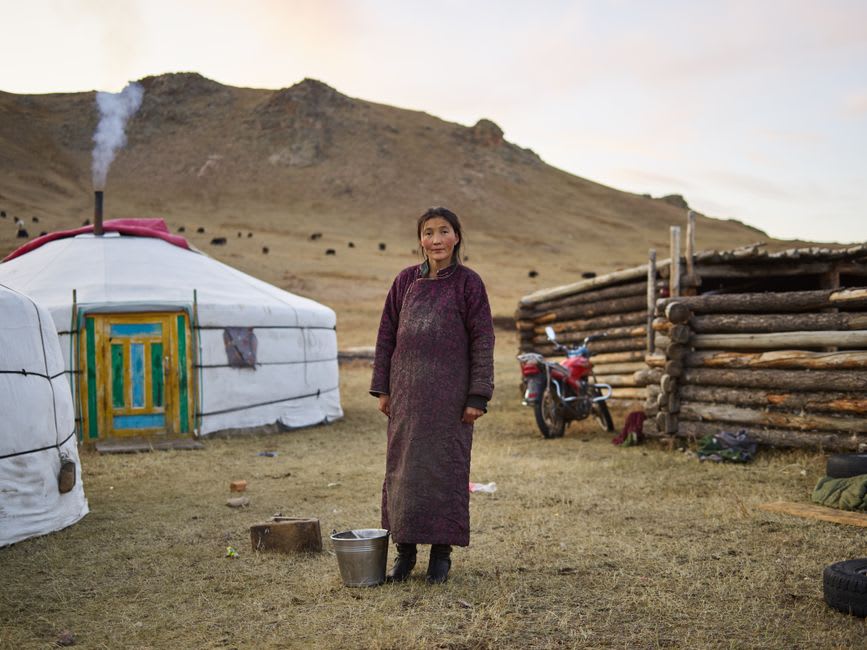 Wooden bathhouse structures with steaming pools set against golden autumn grassland in Arkhangai province