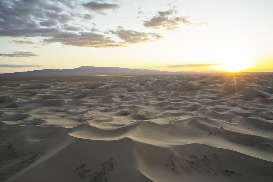 Large rive peu profonde du lac Uvs Nuur avec des montagnes lointaines et une steppe ouverte sous un ciel pâle