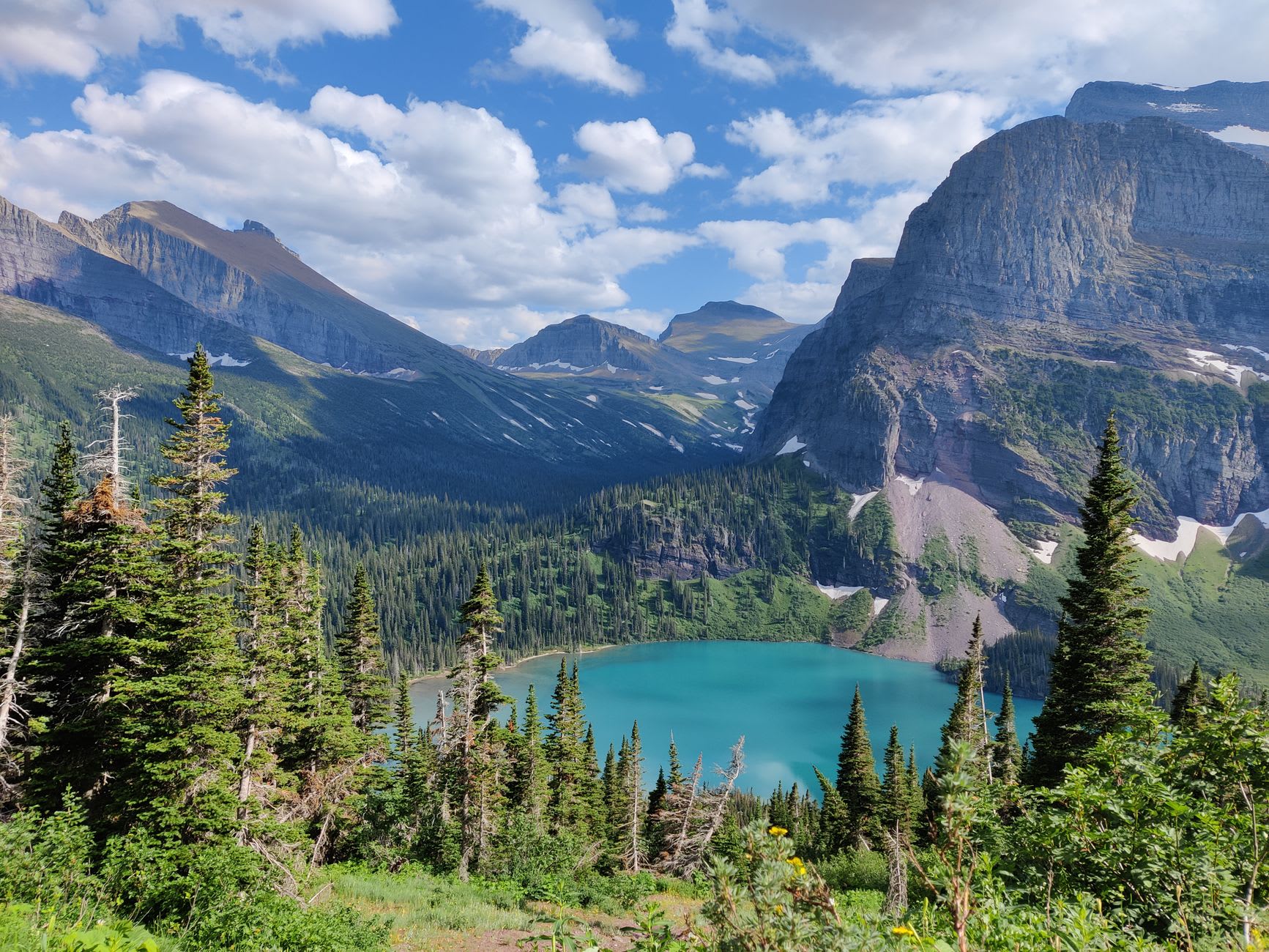 Hikers on the trail to Grinnell Glacier with the glacier's brilliant blue ice visible in the rocky bowl above