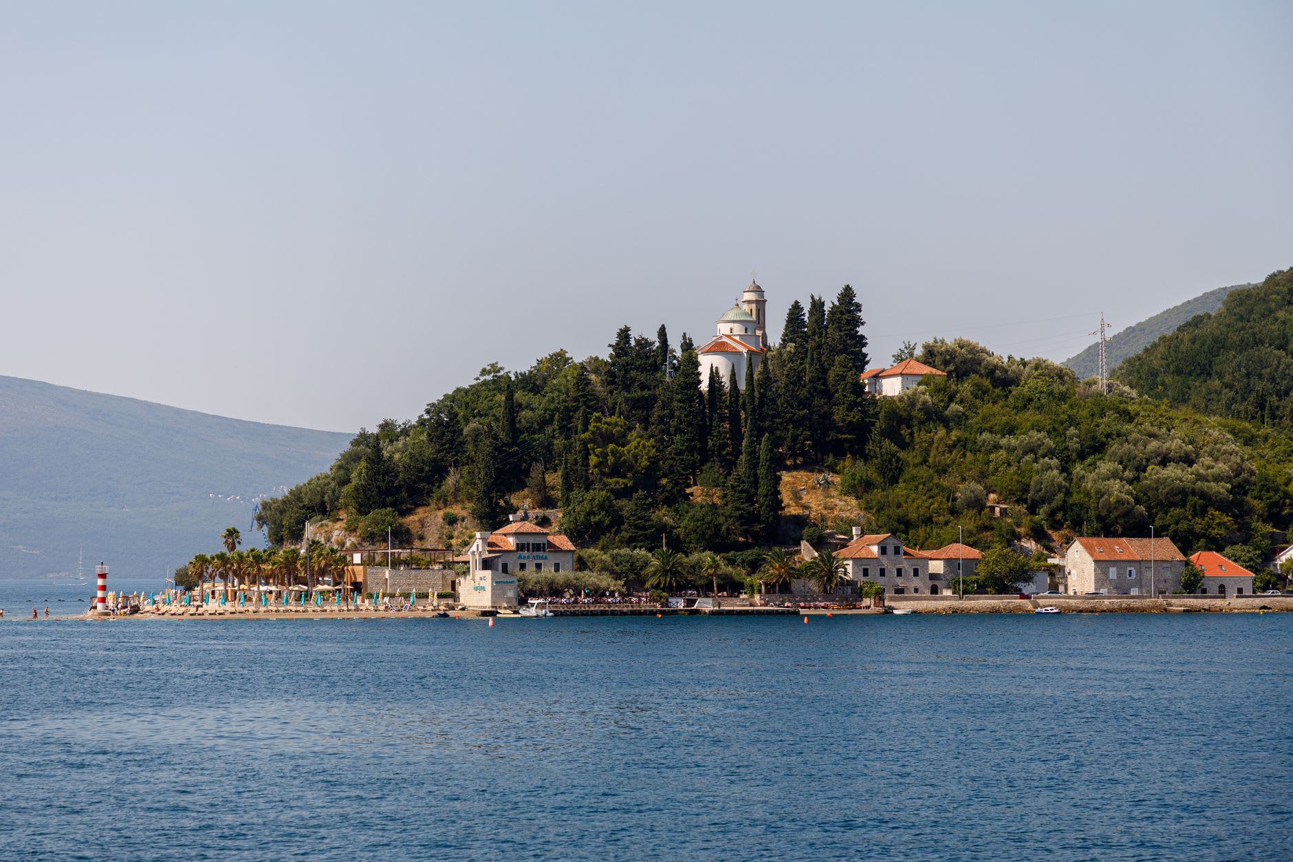 The Old Town of Herceg Novi seen from the bay, white walls and fortress towers above the waterline, bougainvillea spilling down the hillside