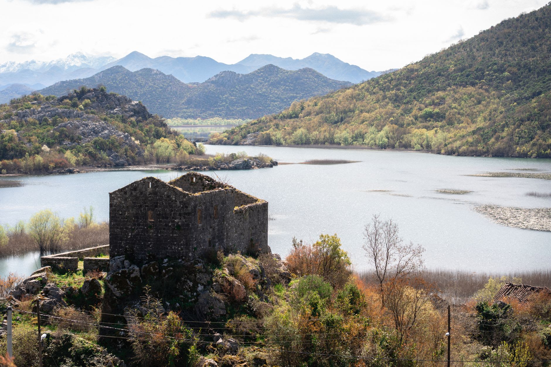 The village of Virpazar at the edge of Lake Skadar, stone houses reflected in calm water, the Albanian mountains rising on the far shore