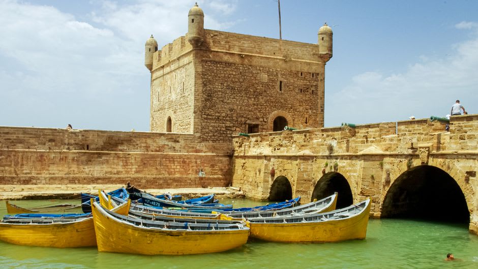 La torre de la fortaleza Sqala du Port sobre los barcos de pesca azules del puerto de Essaouira