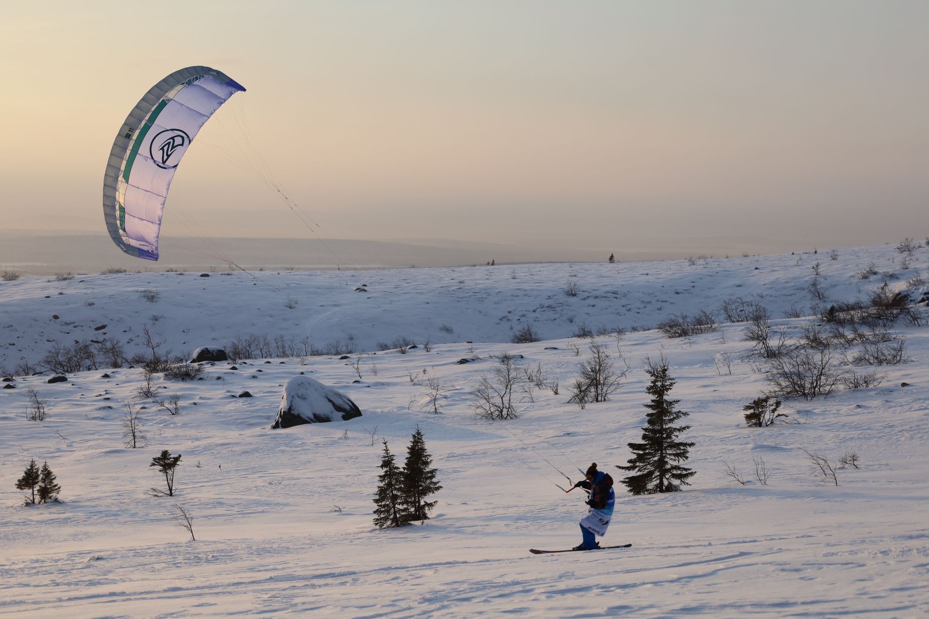 A chairlift rising over snow-covered slopes above Kirovsk, the Khibiny peaks stretching bare and white into low Arctic cloud
