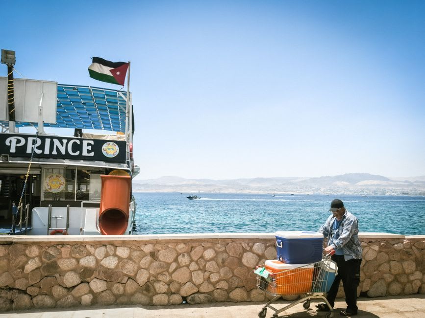 The corniche of Aqaba in late afternoon, fishing boats moored along the waterfront with the mountains of the Sinai peninsula visible across the gulf