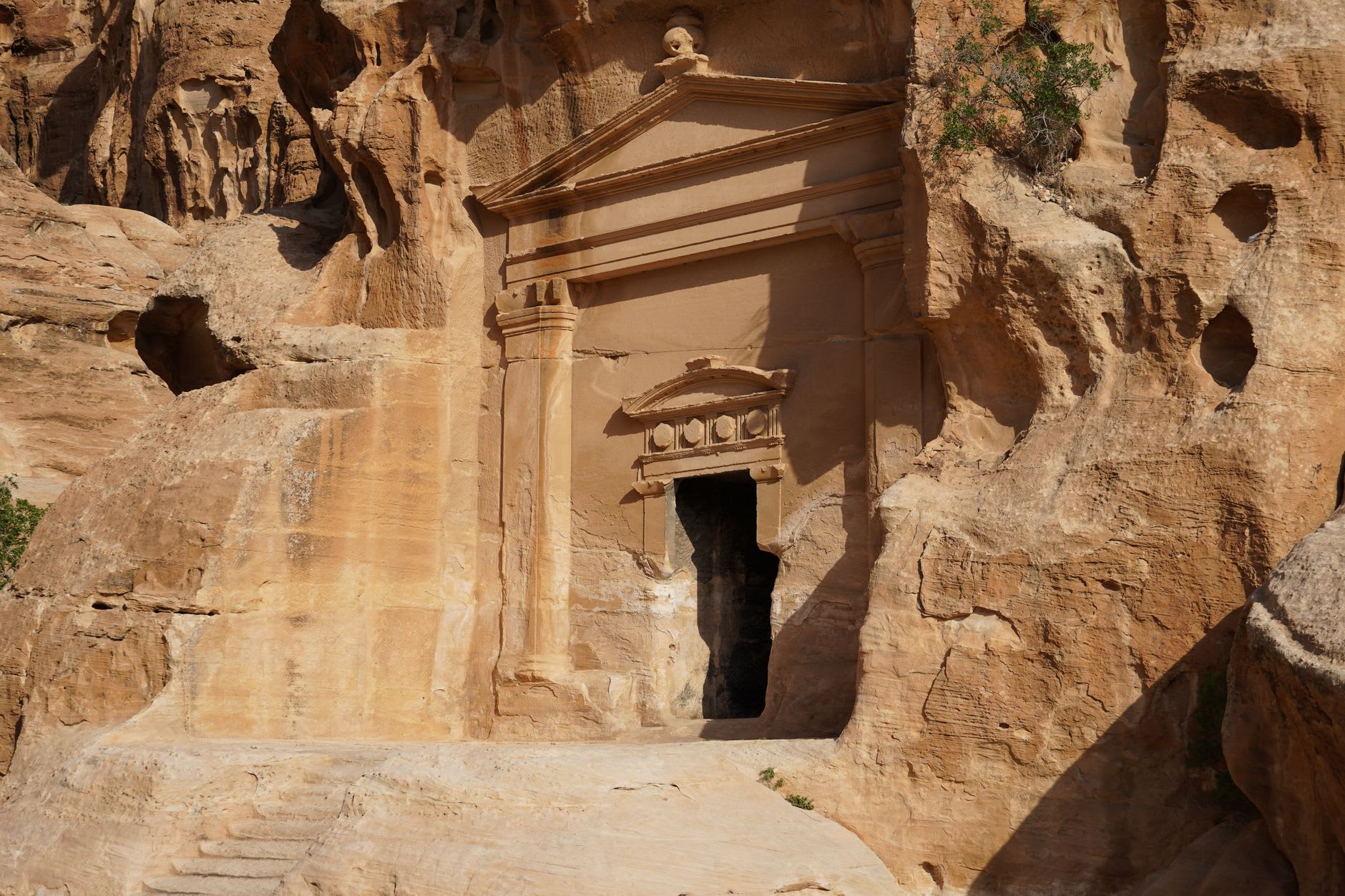 Freestanding Nabataean tomb outcrops rising from flat desert sand at Hegra, their facades carved with elaborate cornices