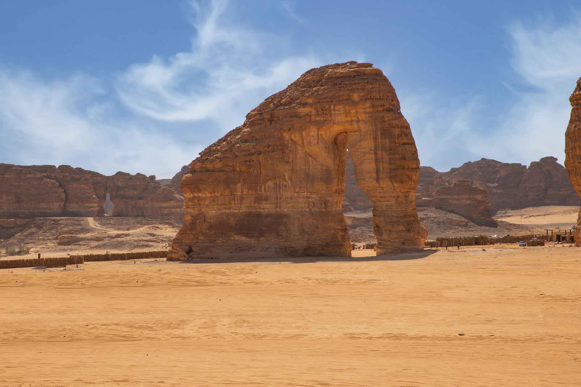 The vast open desert of AlUla at golden hour, Nabataean tomb outcrops scattered across the plain like stone sentinels