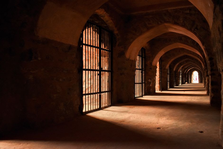 A vaulted stone corridor deep inside Karak Castle, dark basalt archways leading toward a shaft of daylight from an opening above