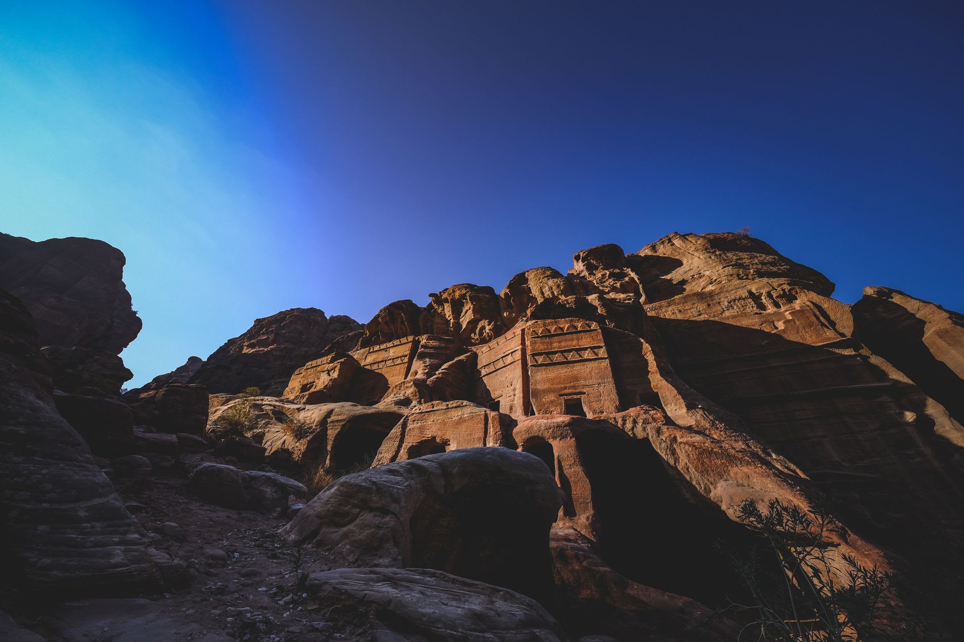 The carved facade of the Urn Tomb at Petra seen from below in afternoon light, its three lower arched chambers and upper classical doorway