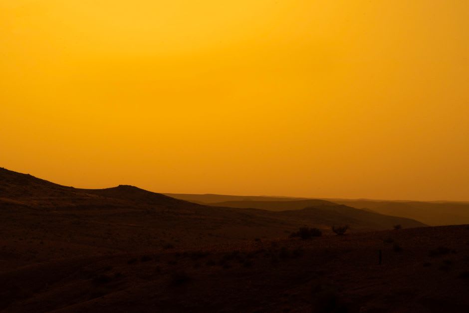 The desert floor of Wadi Araba at sunset, the flat valley glowing deep rust-red with distant mountains turning to silhouette