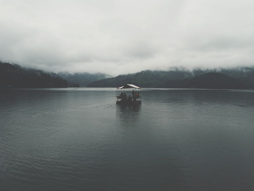 Une barque en bois dérivant sur l'eau verte et immobile du lac Begnas, avec des collines boisées reflétées à la surface