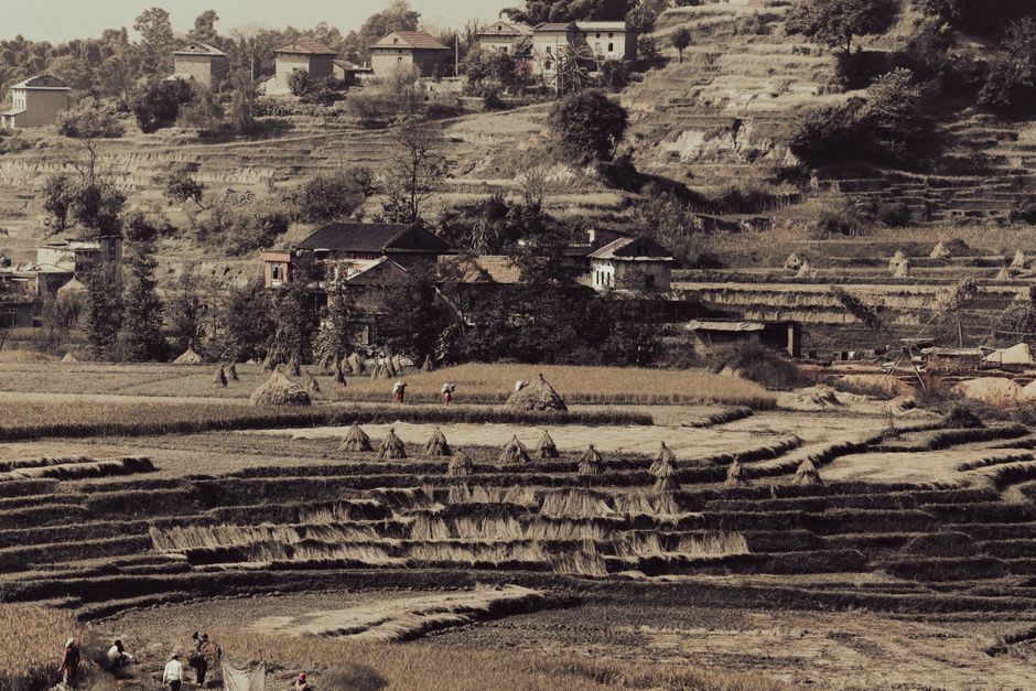 Wide view of Sikles village spread across terraced hillside farmland with stone houses and grazing livestock