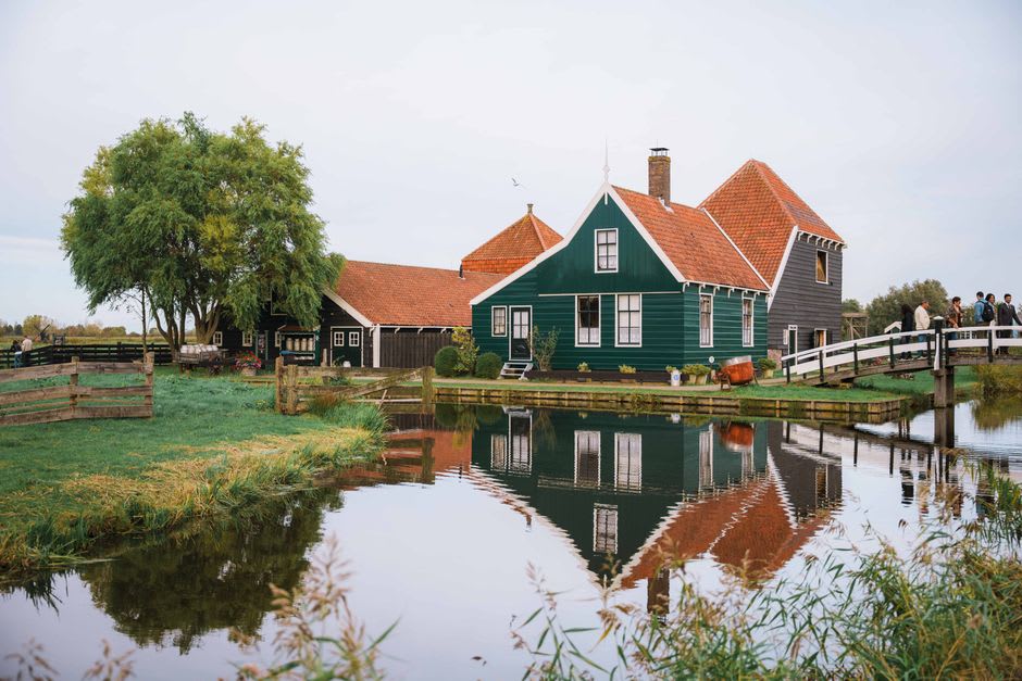 Wooden houses painted dark green lining a canal path at Zaanse Schans