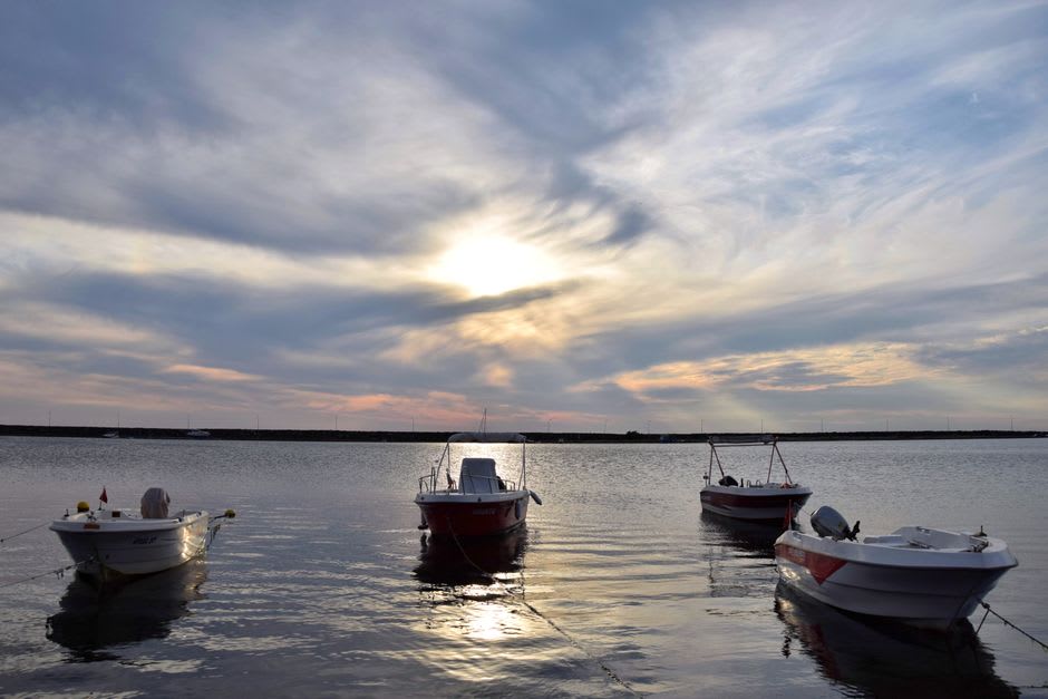 Fishing boats moored in Koumac's working harbour at sunset, nets and gear stacked on the dock