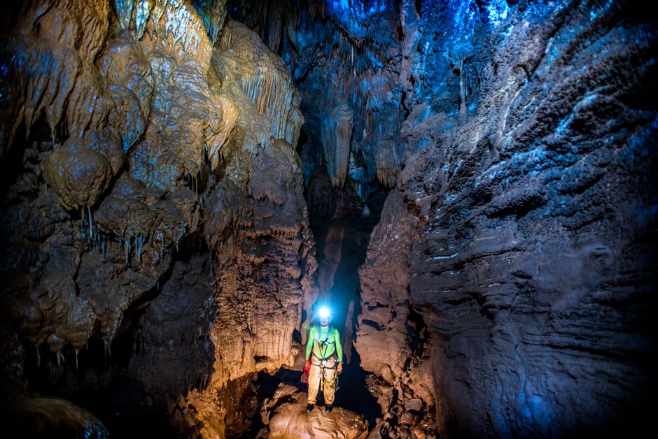 The interior of a Koumac limestone cave lit by headlamp, stalactite formations visible on the ceiling
