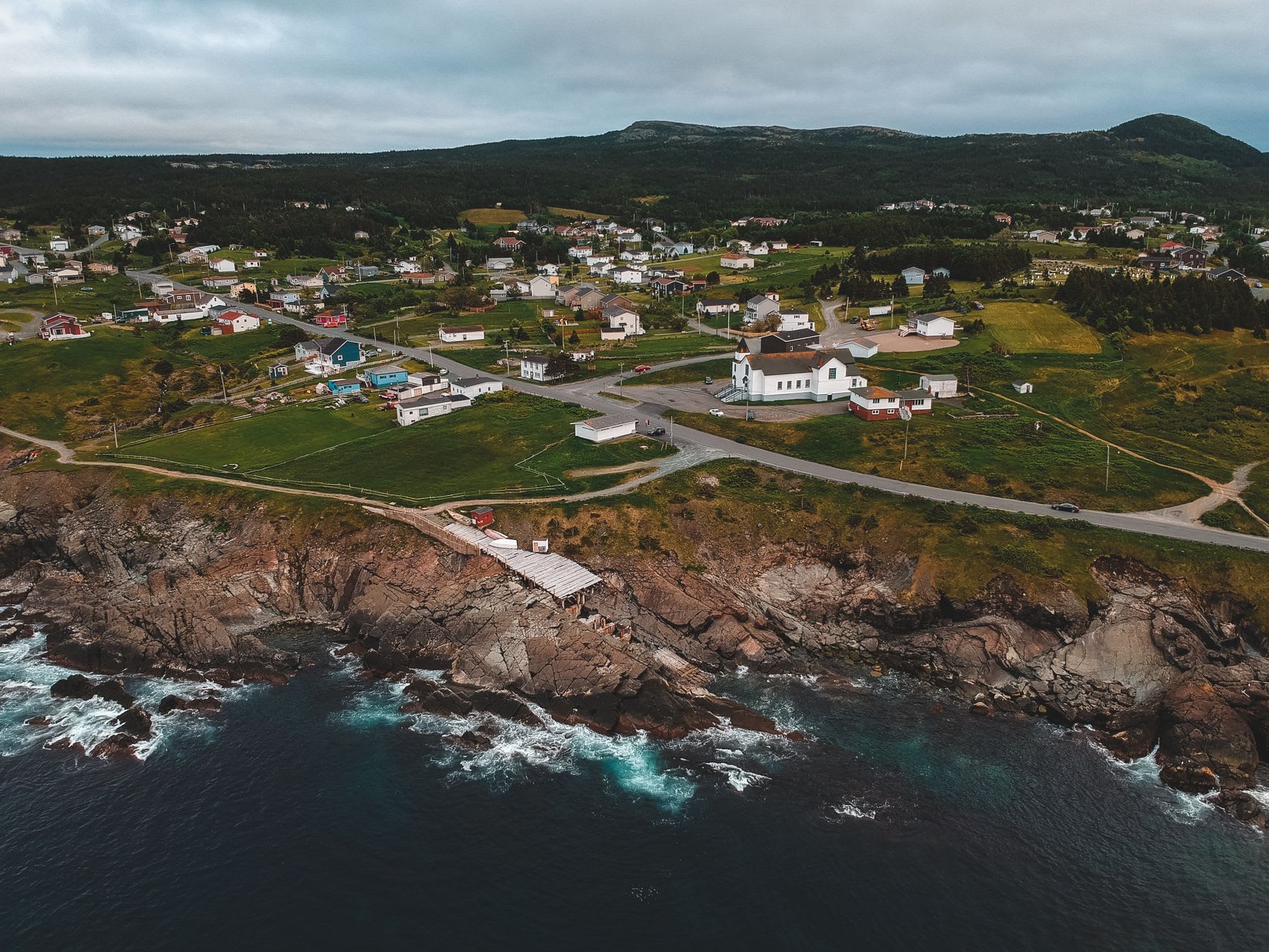 The historic townscape of Bonavista with colourful saltbox houses along the harbour front, grey water stretching beyond