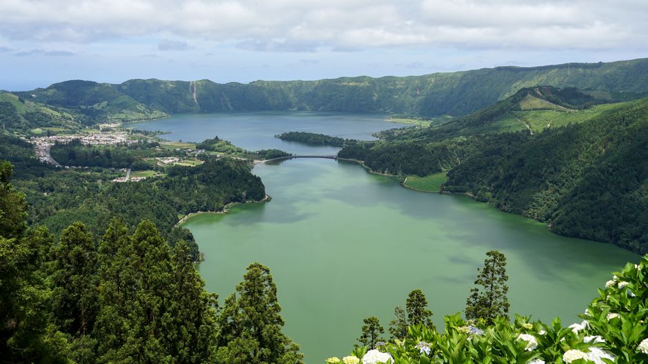 A panoramic view from the rim of Apoyeque showing the crater lake in the foreground and the wide grey expanse of Lake Managua stretching toward the horizon