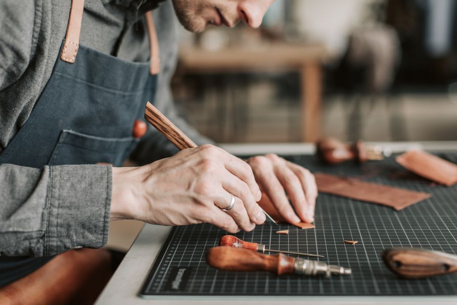 A leatherworker cutting a tooled saddle strap by hand in a Camoapa workshop