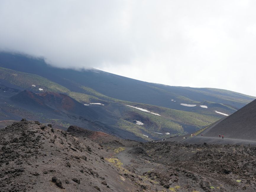 Hikers climbing the black cinder slope of Cerro Negro with boards strapped to their backs