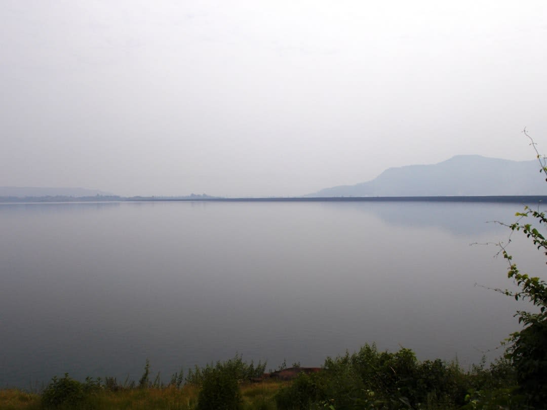 Embalse del Lago Apanás con botes de pesca en aguas calmas y montañas cubiertas de niebla desvaneciéndose al fondo