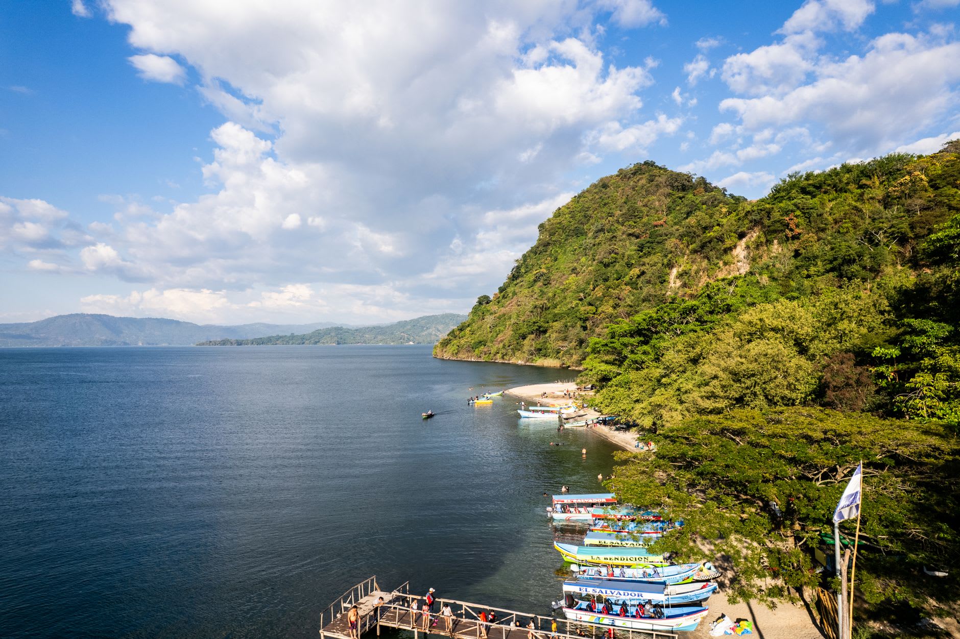 A wooden dock reaching into the still blue water of Laguna de Apoyo with forested crater walls behind