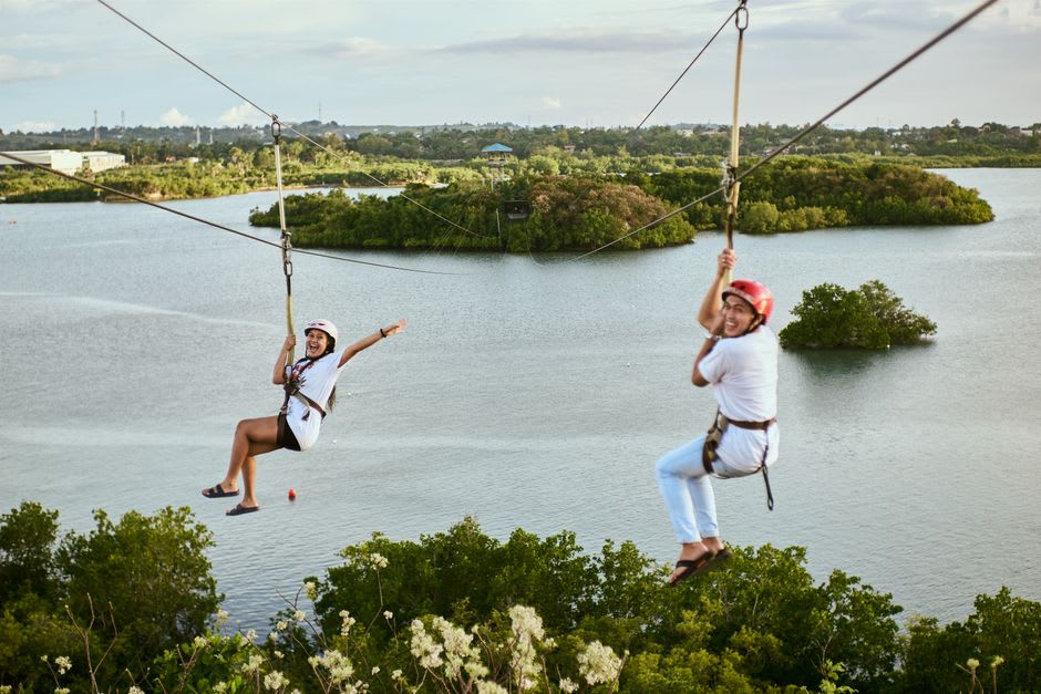 A person zip-lining across Laguna de Tiscapa, suspended above the still green water with the crater's forested walls on either side