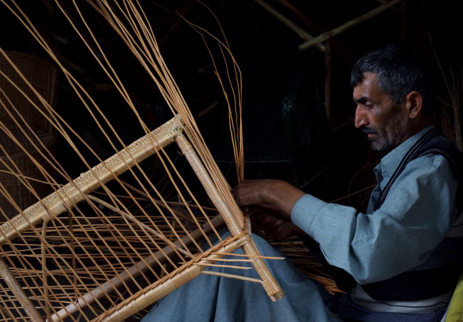A craftsman weaving wicker cane onto a wooden rocking chair frame