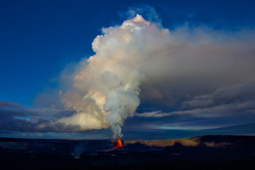 Visitors standing at a railed viewing platform peering down into the glowing lava lake of Masaya's active crater at night