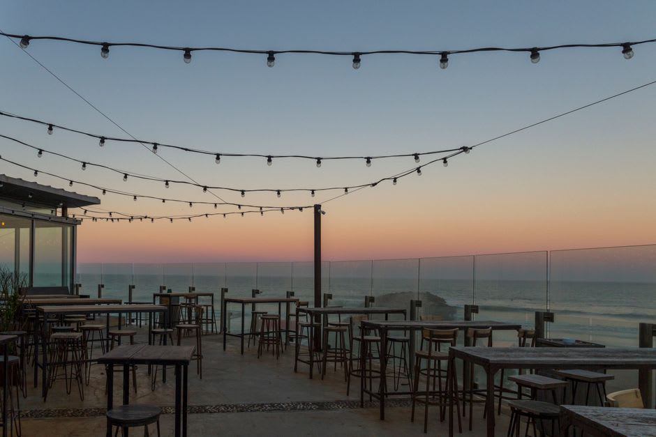 Bar de playa con luces de cadena frente al océano en Playa Maderas