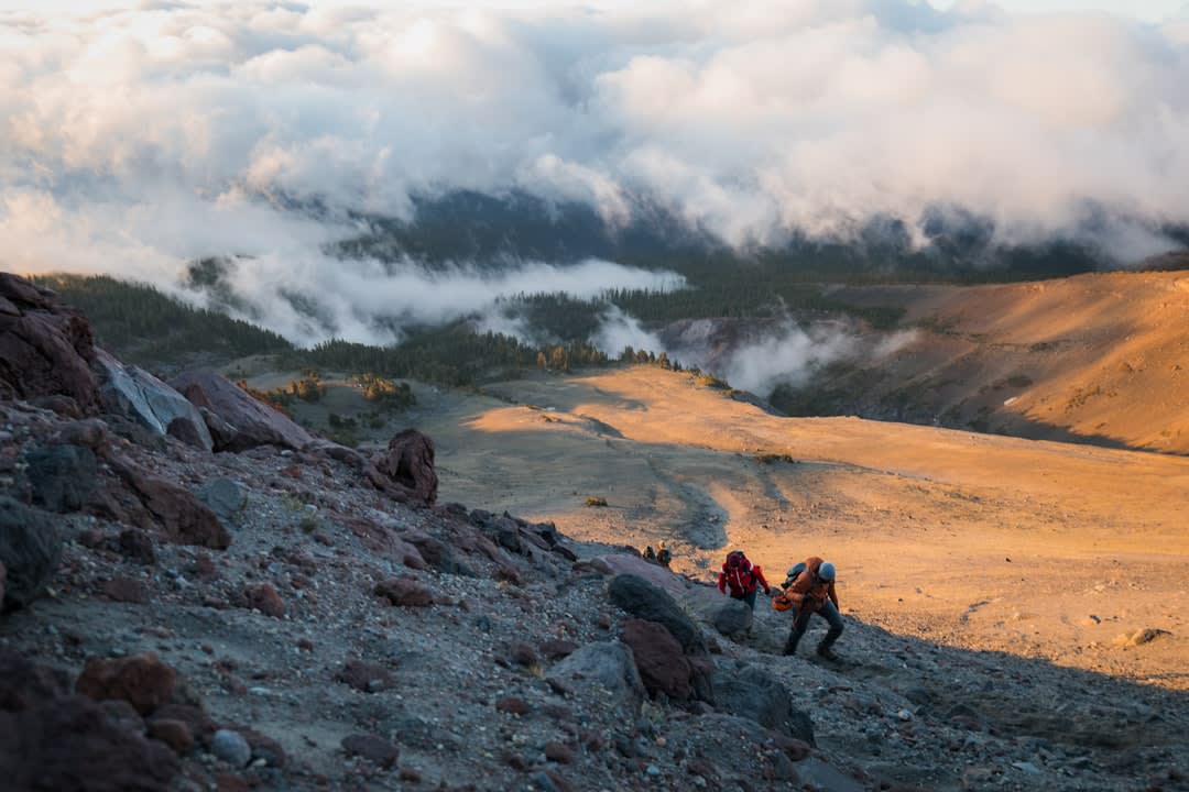 Excursionistas ascendiendo una ladera empinada cubierta de ceniza cerca de la cumbre del Volcán Concepción, con nubes cubriendo el cráter arriba