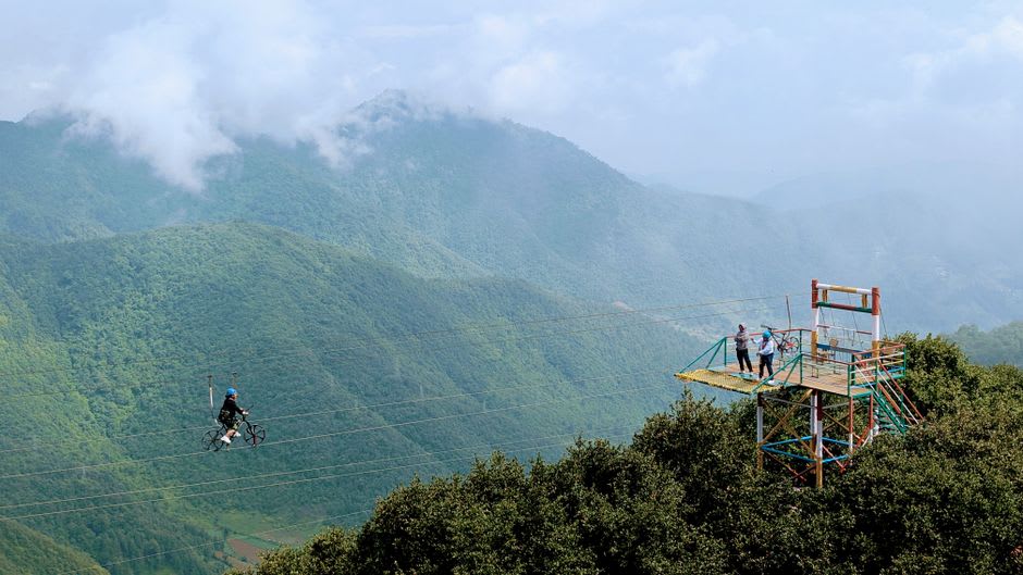 Un excursionista en una plataforma de dosel suspendida en el Volcán Mombacho, rodeado de árboles de bosque nuboso cubiertos de musgo con pequeñas flores de orquídea visibles en una rama cercana