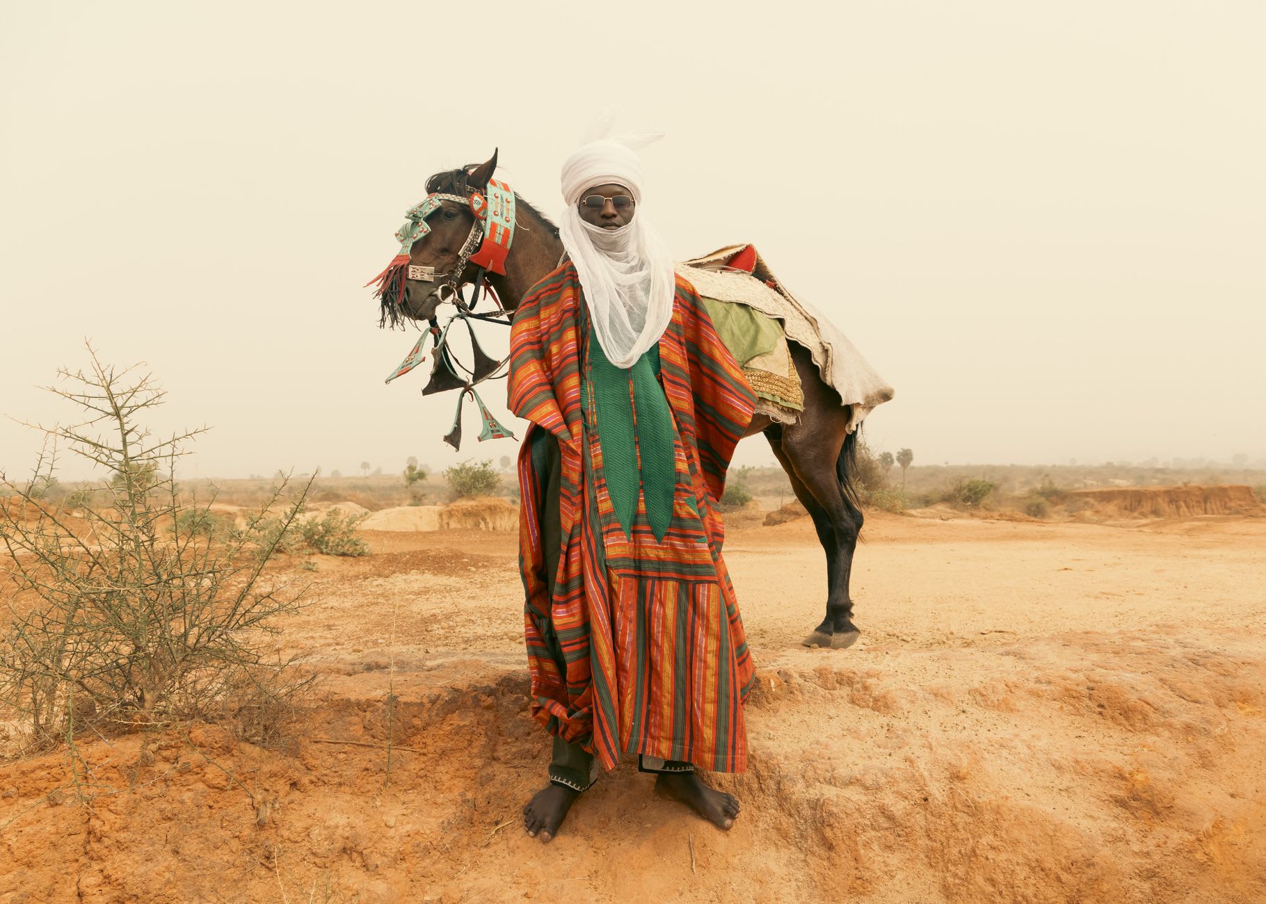 Los campamentos de tiendas de nómadas tuareg extendiéndose por la llanura a las afueras de In-Gall al amanecer, con humo de hogueras ascendiendo en el aire quieto