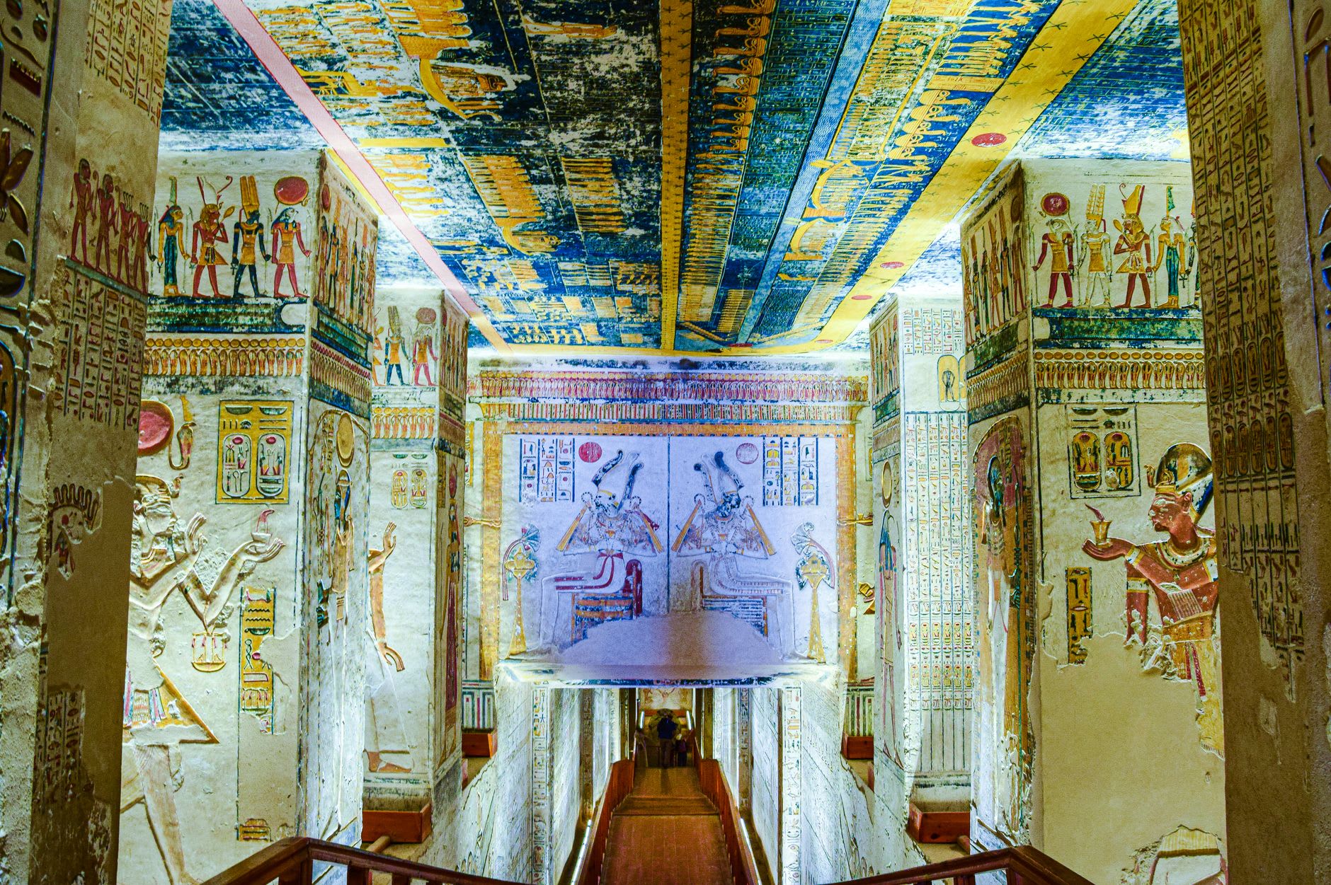 The narrow entrance path descending into one of the royal tombs, painted walls visible in the electric light beyond the threshold