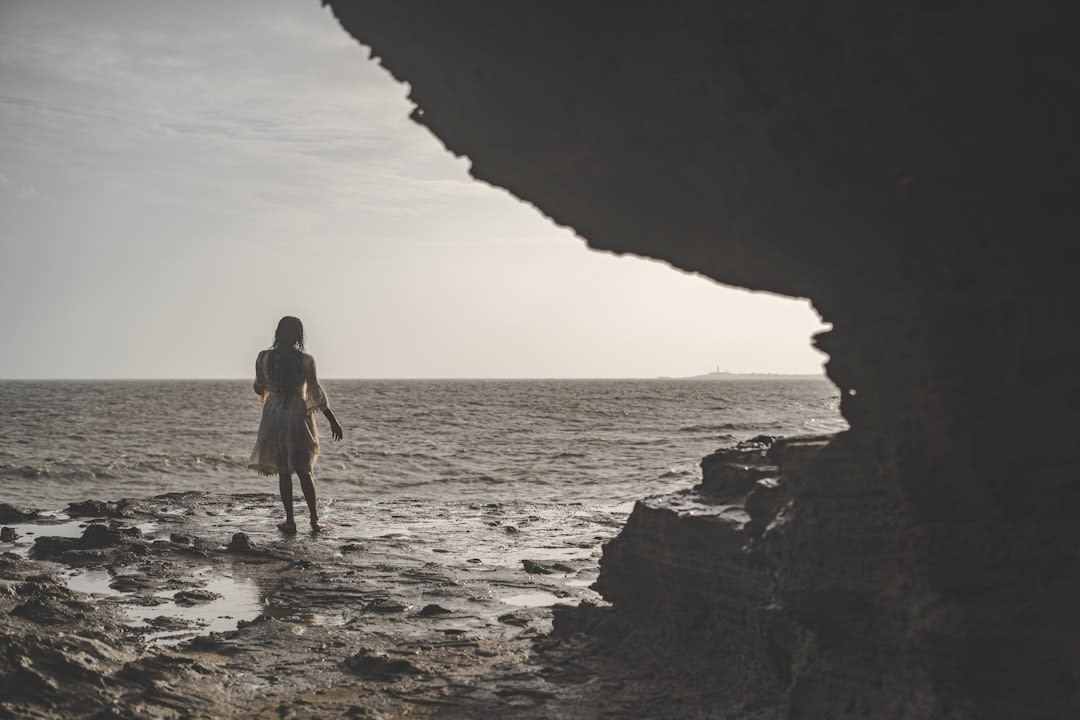 Lia standing at the edge of the brackish pool inside Anapala Chasm, dwarfed by the limestone walls