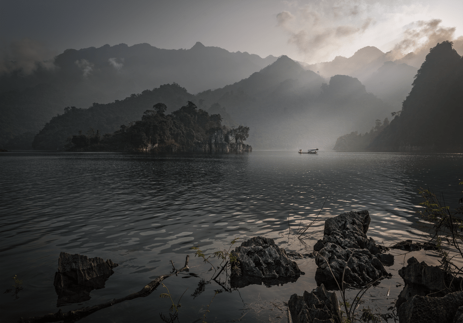 Wooden boat gliding across Ba Be Lake with limestone cliffs rising from the water
