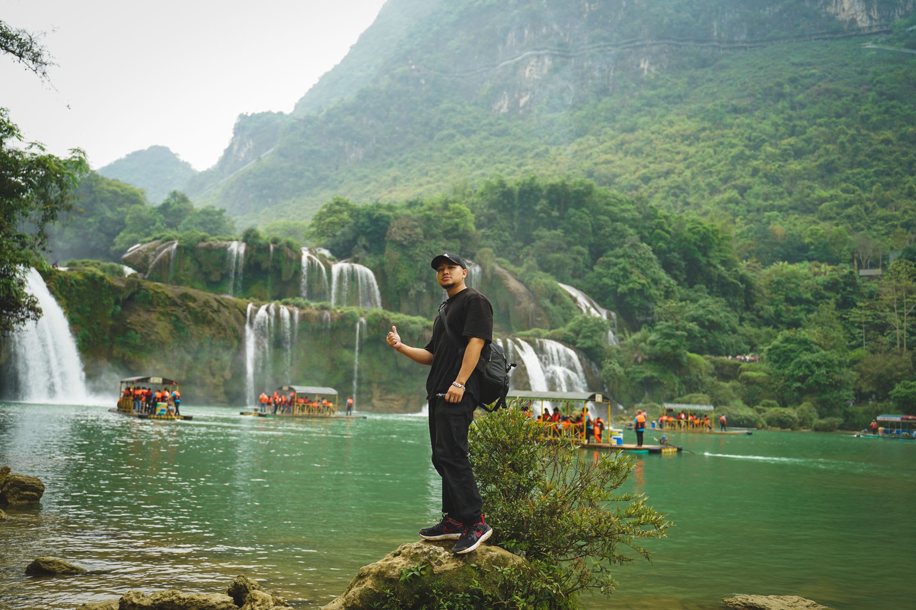 The tiered limestone shelves of Bản Giốc waterfall at lower water level, the layered rock visible behind the flow, forest dark green on the cliff above