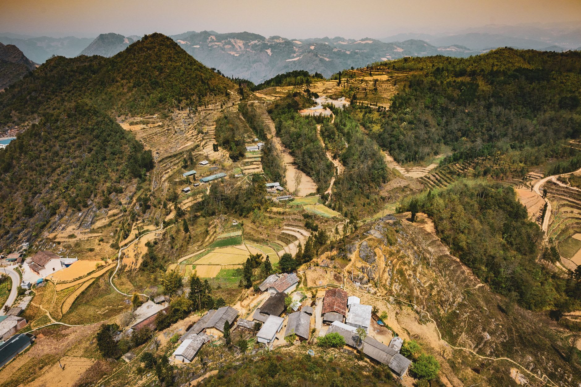 The Lo River winding through Ha Giang's valley floor, limestone peaks rising behind, a woman on a bicycle crossing the bridge