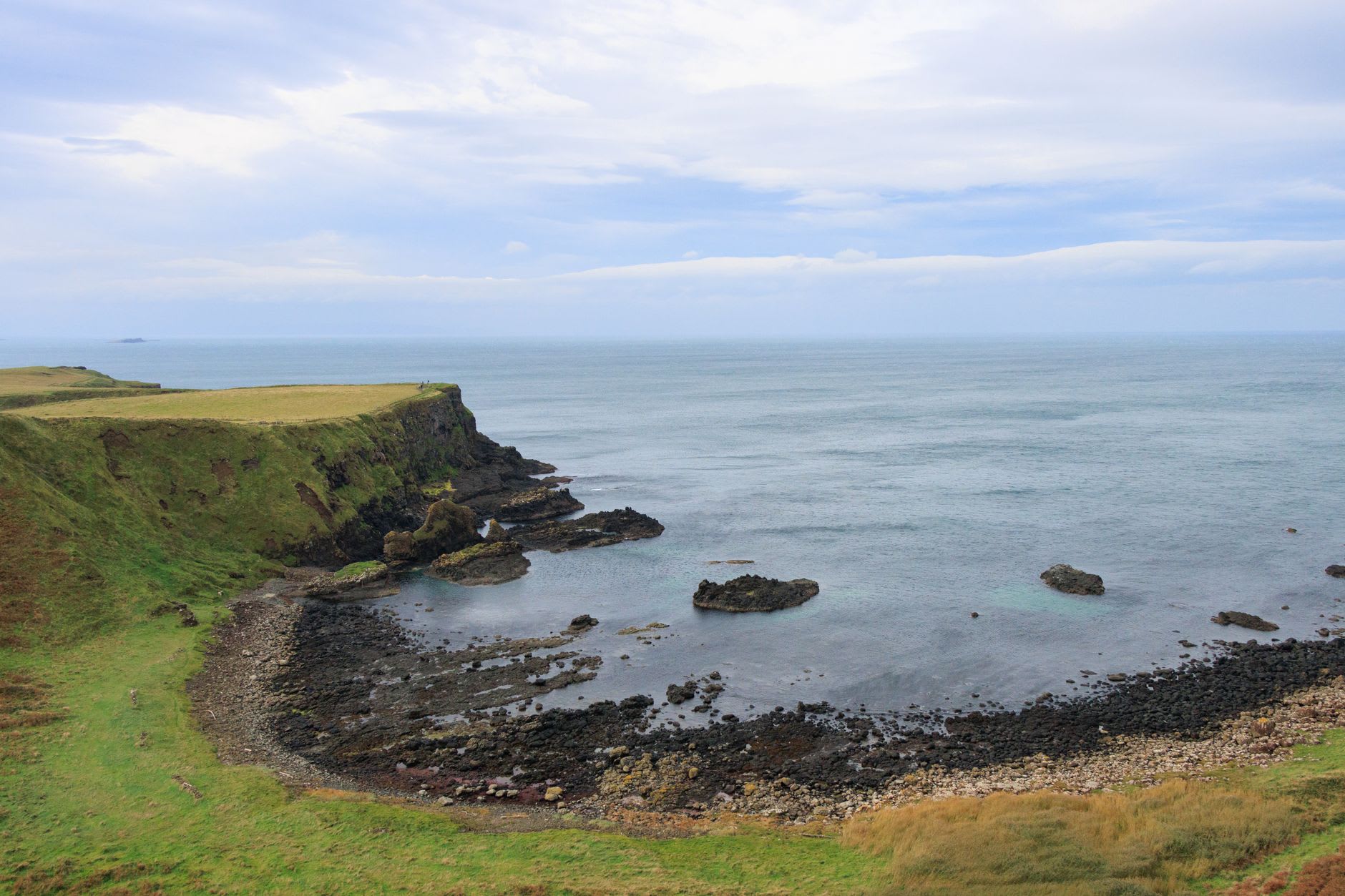 The ruined inner ward of Dunluce Castle seen from the mainland, stone towers rising against the ocean with basalt cliffs below